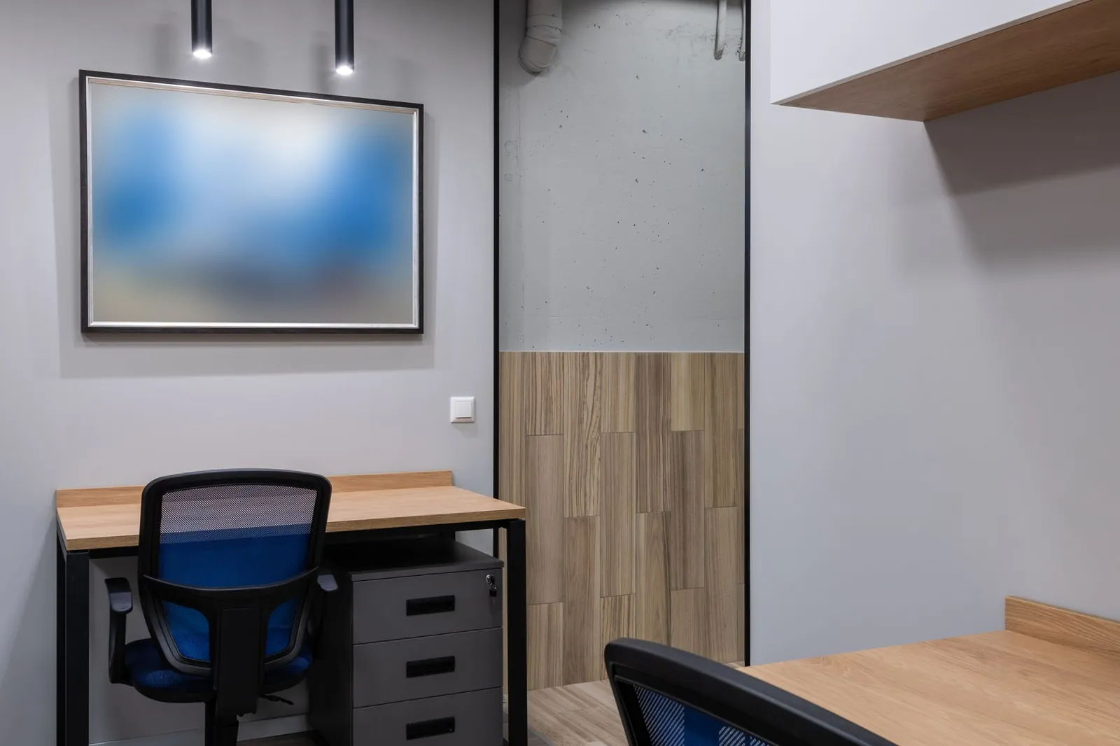 A small office with pale grey walls, a wood desk and a blue office chair